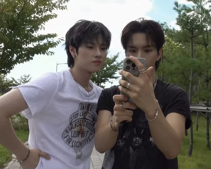 Cassius and Natha looking at a phone beneath the trees